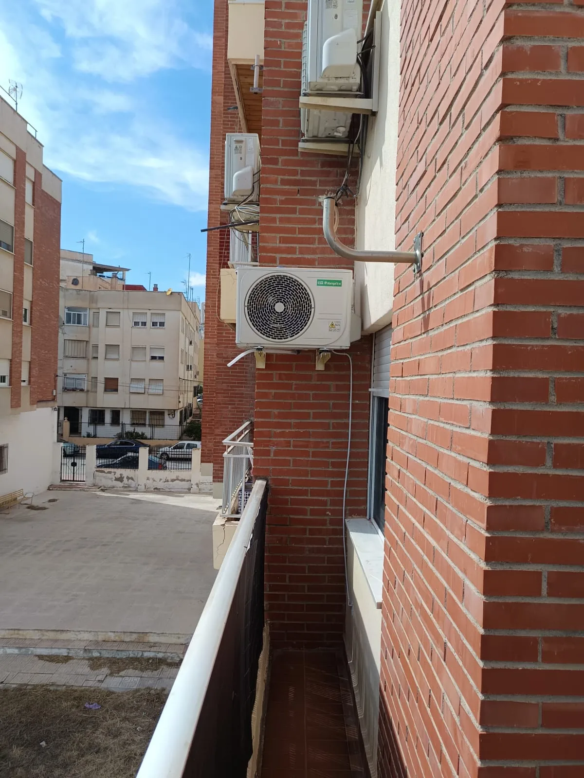Unidad exterior de aire acondicionado instalada en la fachada de ladrillo de un piso.