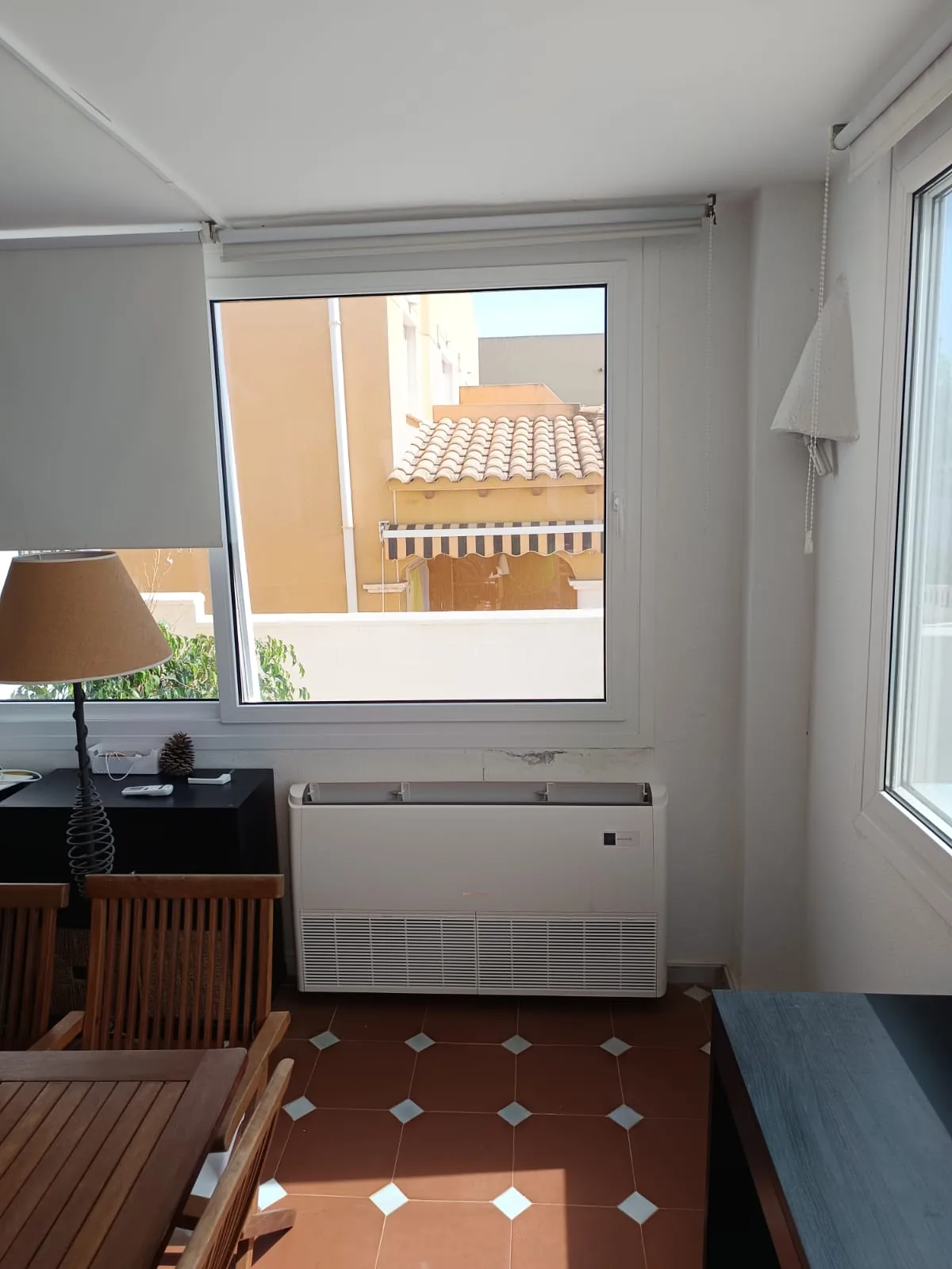 Equipo de aire acondicionado de consola suelo-techo instalado bajo la ventana de una vivienda.