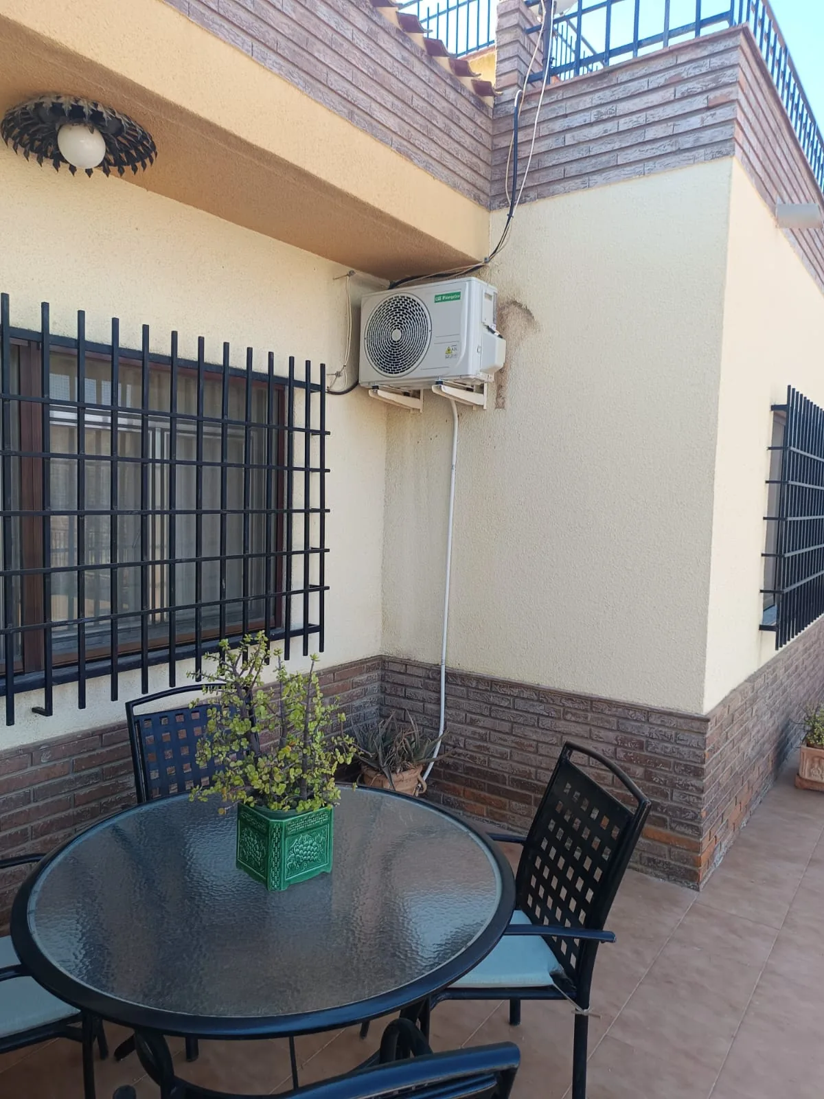 Unidad exterior de aire acondicionado instalada en la terraza, junto a la mesa donde se come fuera.