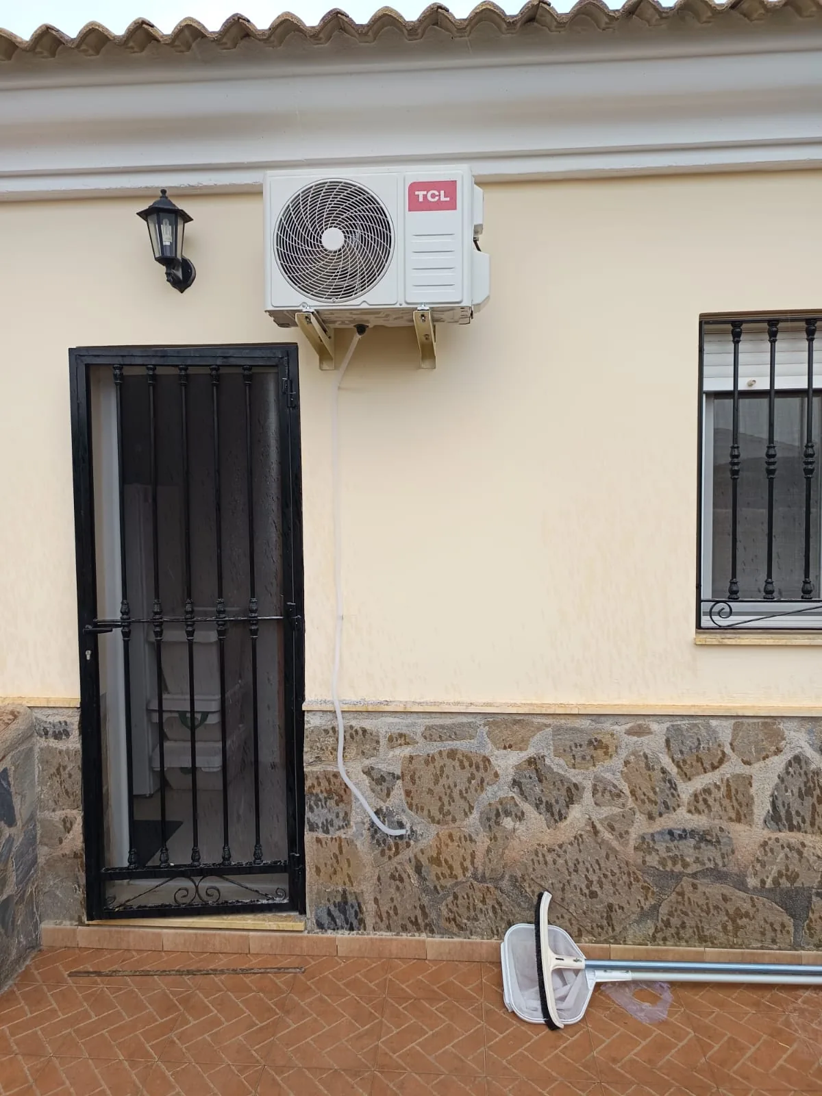 Outdoor air conditioning unit fitted to the façade of a village house with barred windows.