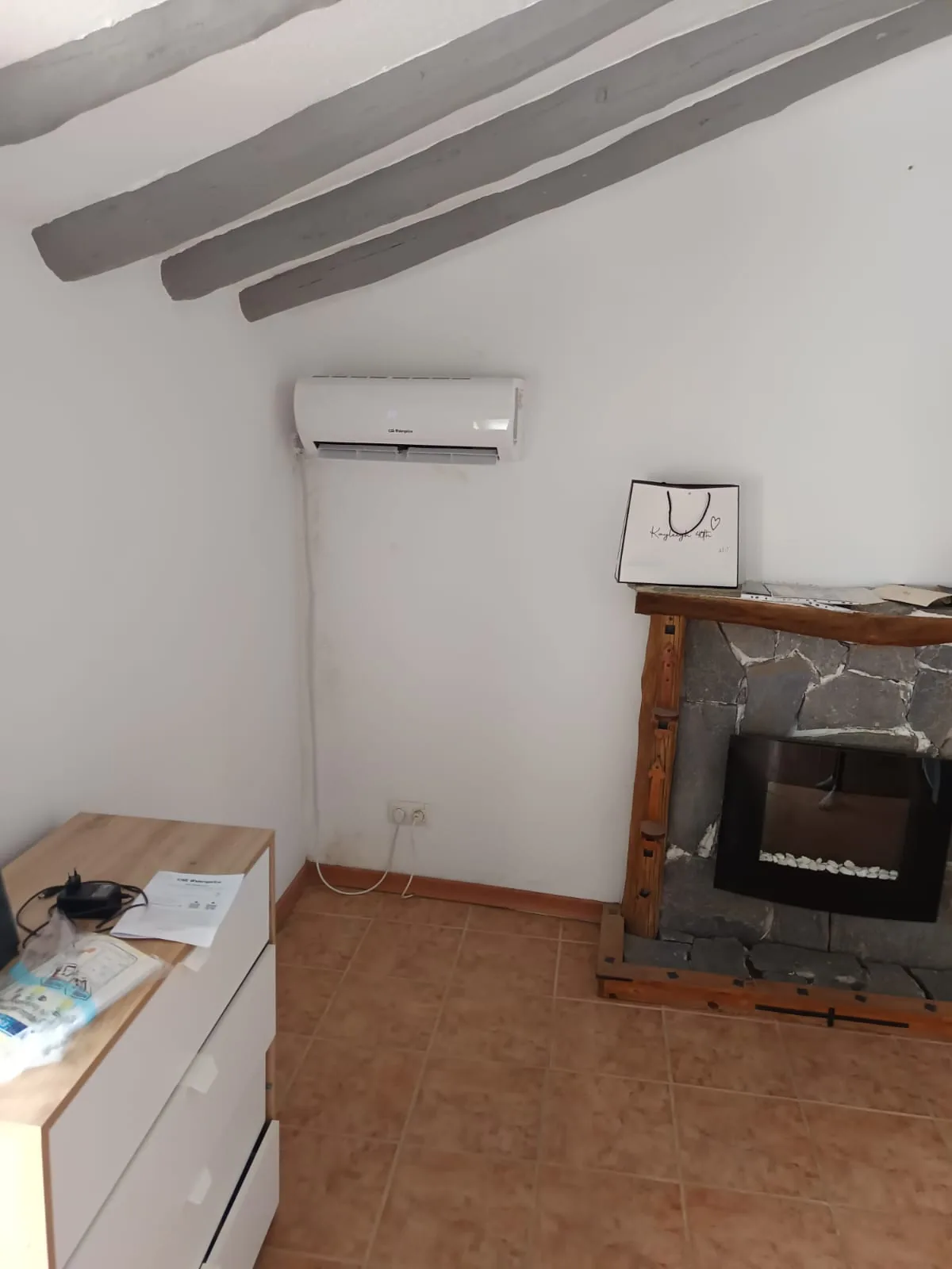 Wall-mounted air conditioning unit fitted in the living room of a country house with exposed wooden beams.