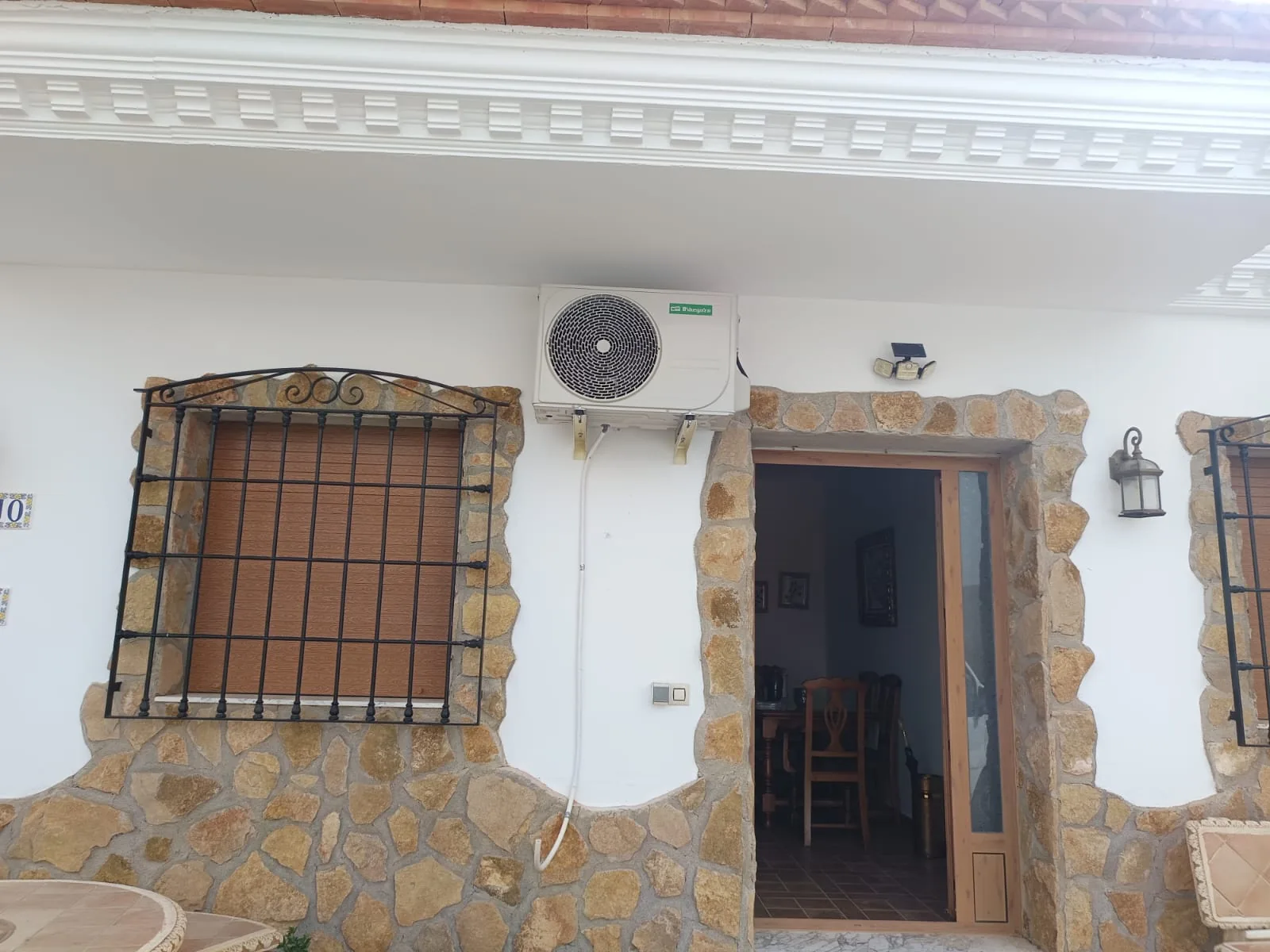 Unidad exterior de aire acondicionado en la fachada de piedra de una vivienda.