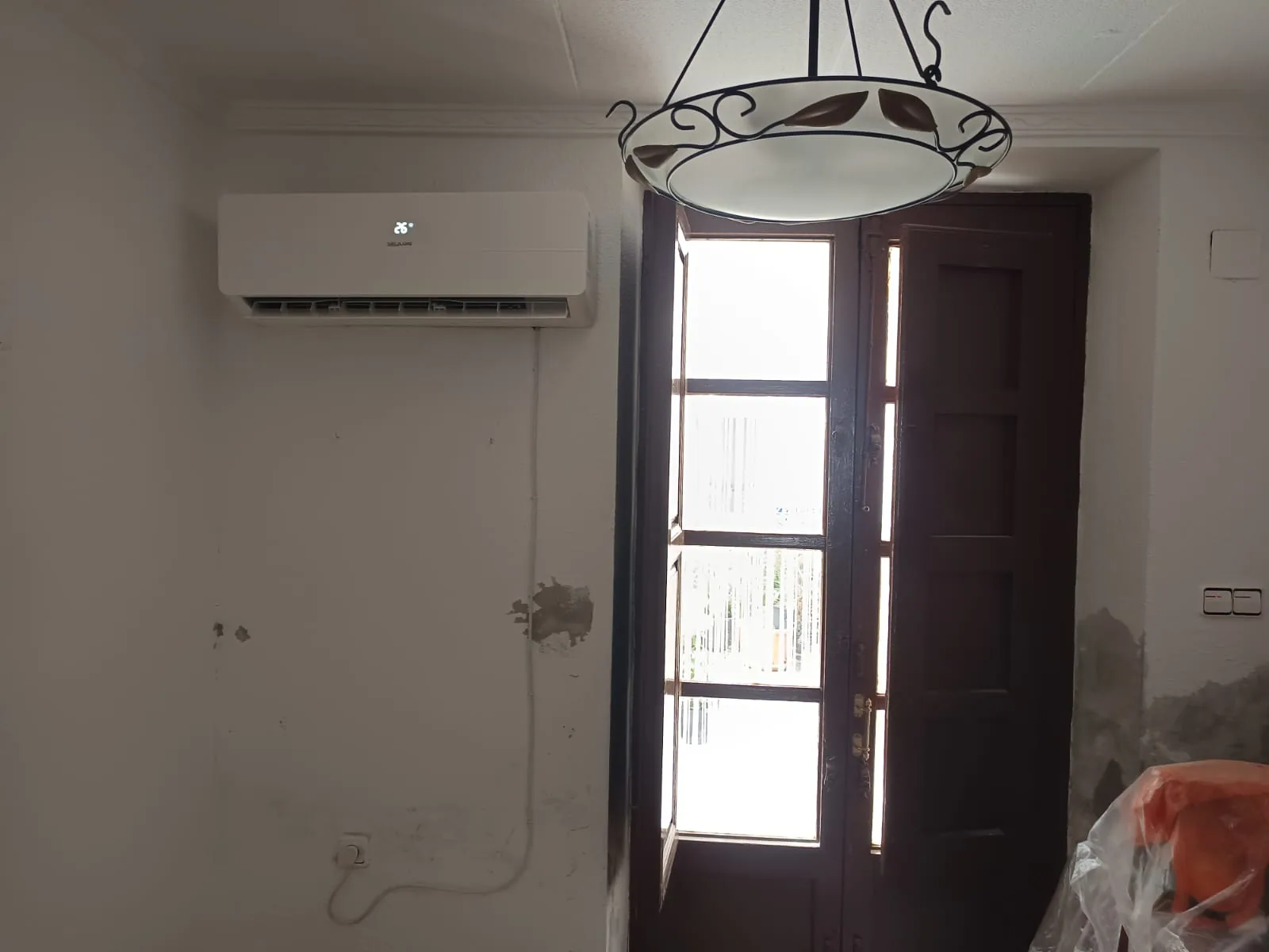 Aire acondicionado instalado en la pared de un salón, junto a la puerta de madera.