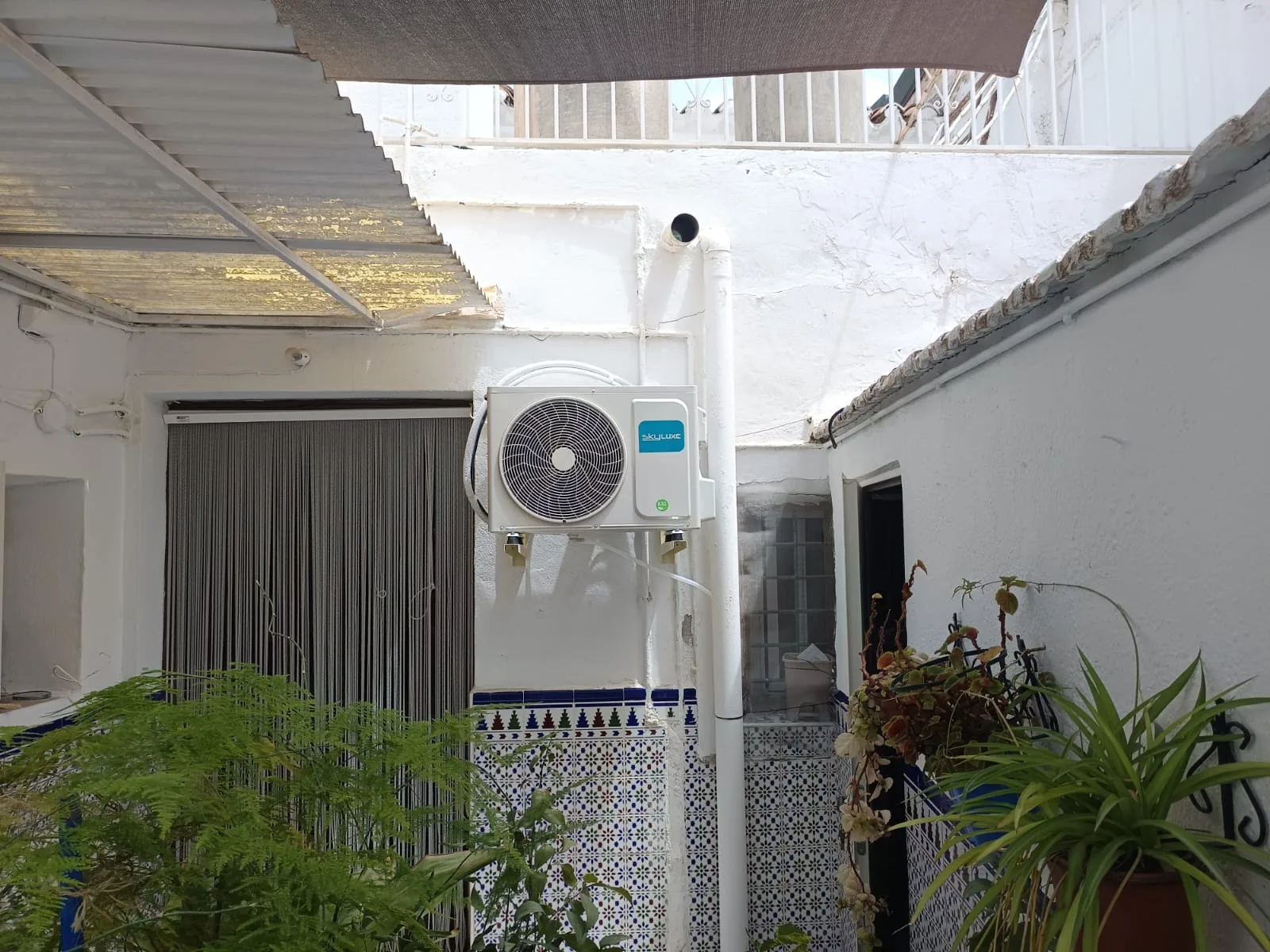 Unidad exterior de aire acondicionado instalada en un patio con plantas.